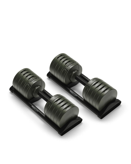 NÜOBELL S 240 adjustable dumbbells in olive green finish resting on black trays, showing the rotating plate design and twist-handle mechanism with weight markings visible on the stacked plates.