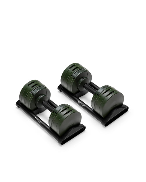 NÜOBELL S 224 adjustable dumbbell pair resting in black storage trays on a white background, showcasing the deep olive-green layered weight plates, knurled aluminum handles, and twist-dial selectors with visible weight markings on each end.