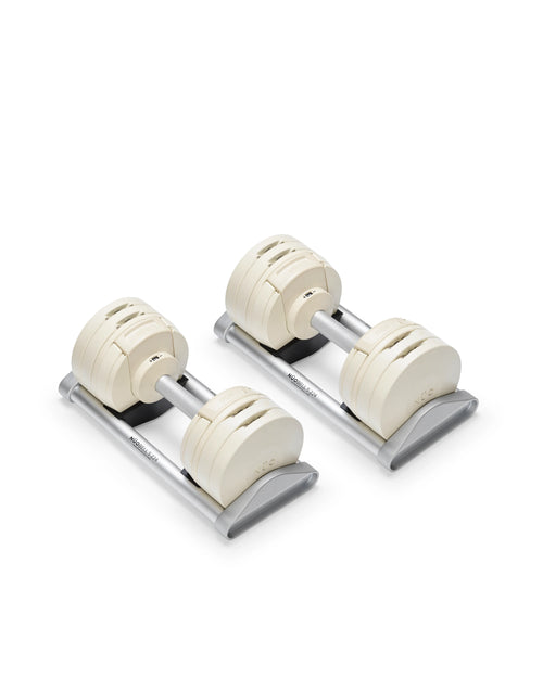 NÜOBELL S 224 adjustable dumbbell pair resting on compact gray trays, showcasing the patented twist-dial selection system and cream-colored weight plates with flat-head construction.